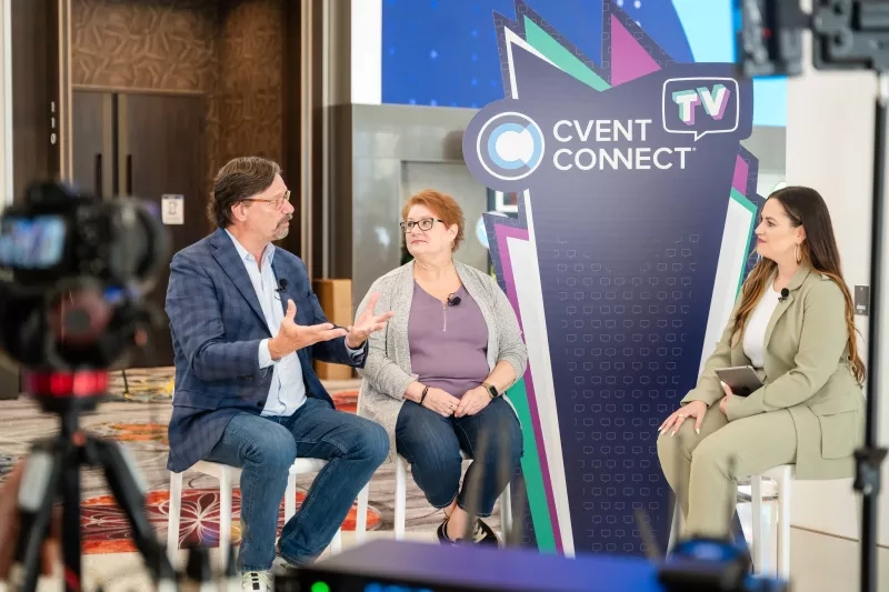 Three people sit on stools in front of a Cvent Connect TV sign in front of a camera.