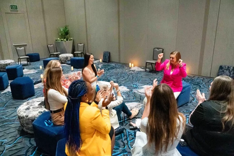 Women in a room with round seating, candles, and a woman speaking at the front.