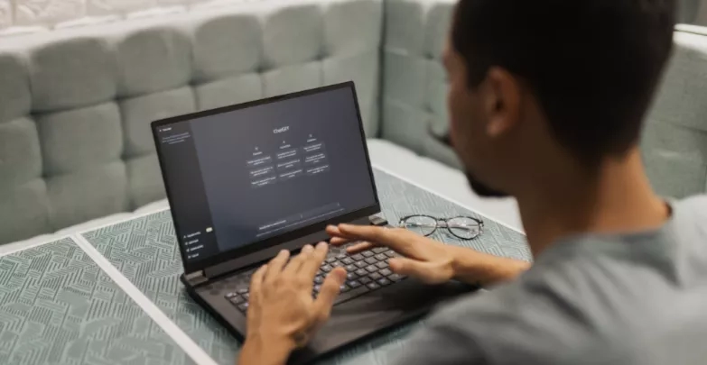 Man using a laptop to type on chat gbt in a coffee shop.