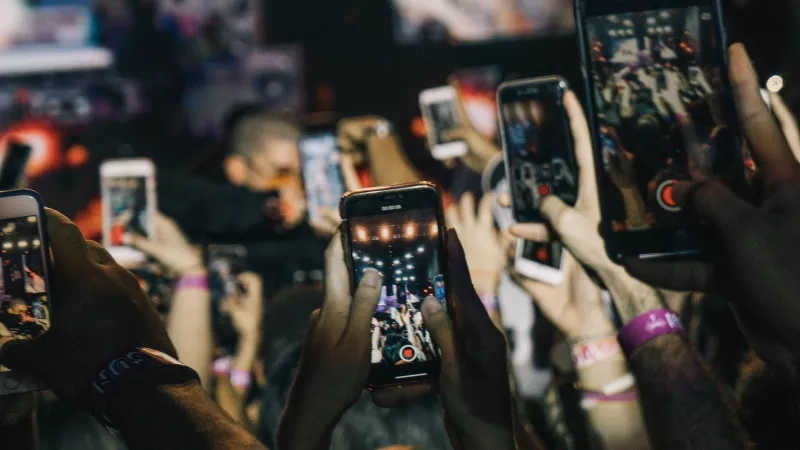 A crowd of people at an event, capturing videos and photos with their phones.