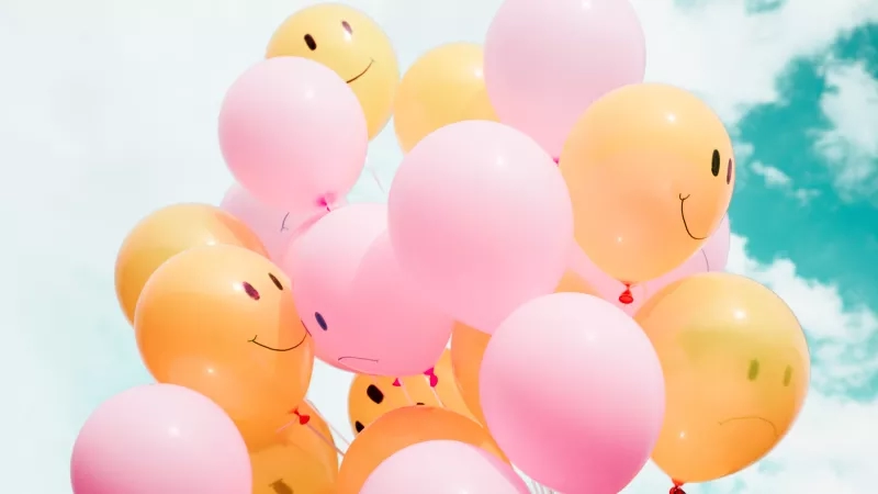 A collection of pink and yellow balloons with smiley faces printed on them against the blue sky.