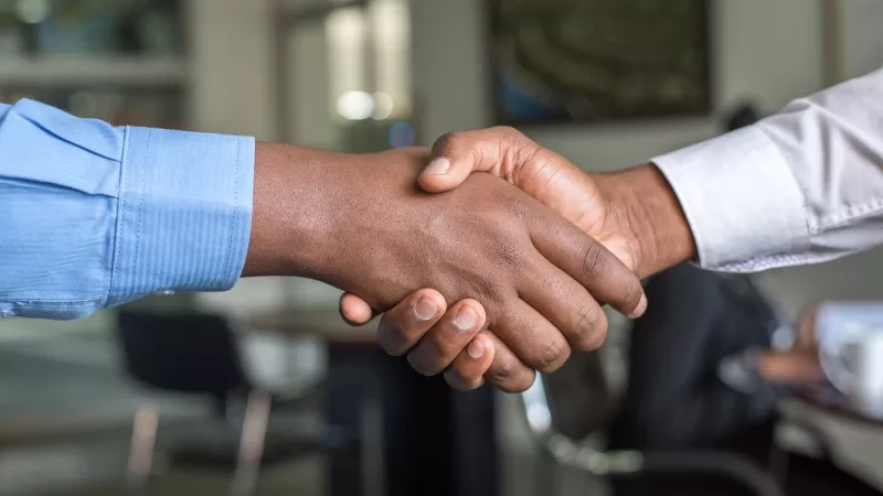 Two people shaking hands in a corporate office to seal a sponsor agreement.
