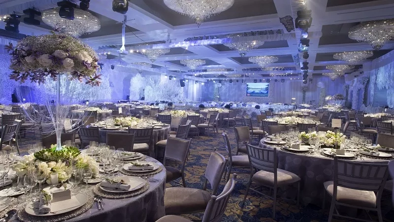 The Mulia Bali Grand Ballroom is set for a formal event with a large chandelier and floral centerpieces.