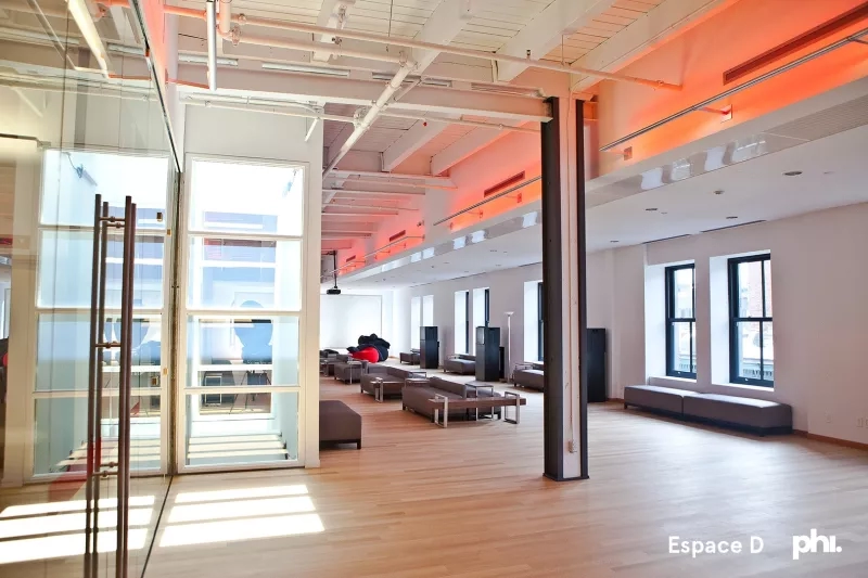 A bright room with many couches, windows, and an open door at Phi Centre in Montreal.