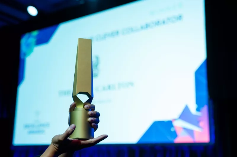 A hand holds up a golden award in front of a screen at Cvent CONNECT 2023.