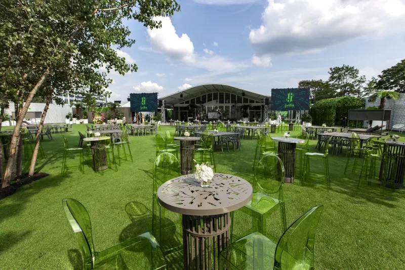 A green outdoor restaurant with tables, chairs, a stage, and a green sign that reads "jardin".