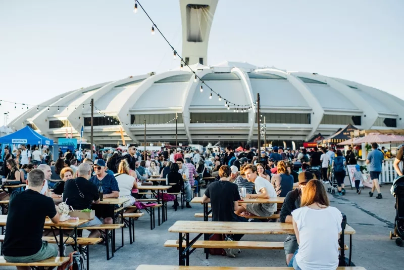 Crowded seating at ÎleSoniq with a white building and glowing lights hanging above the tables.