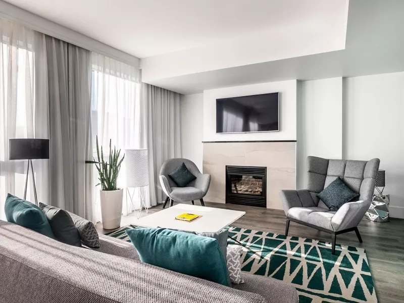 Living room with fireplace, sofa, chairs, TV, coffee table, lamp, curtains, and potted plant in hotel room.