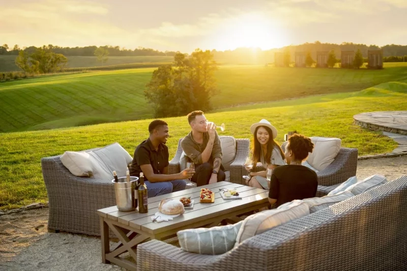 Four people sit on wicker couches, enjoying wine and snacks as the sun sets at Stone Tower Winery.