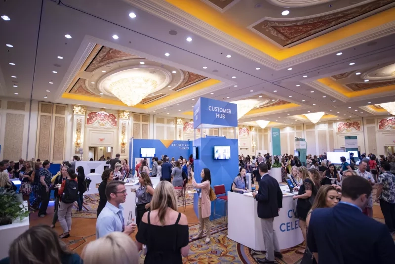 A trade show with booths, a crowd, and a customer hub sign, and a chandelier.