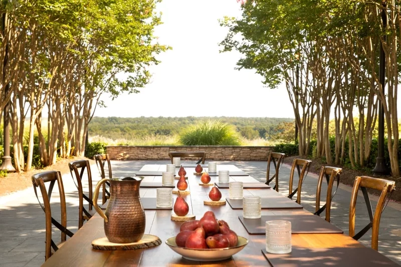 Outdoor meeting with chairs, table, pears, pitcher, candles, trees, stone wall, and lush greenery at the Four Seasons Austin.
