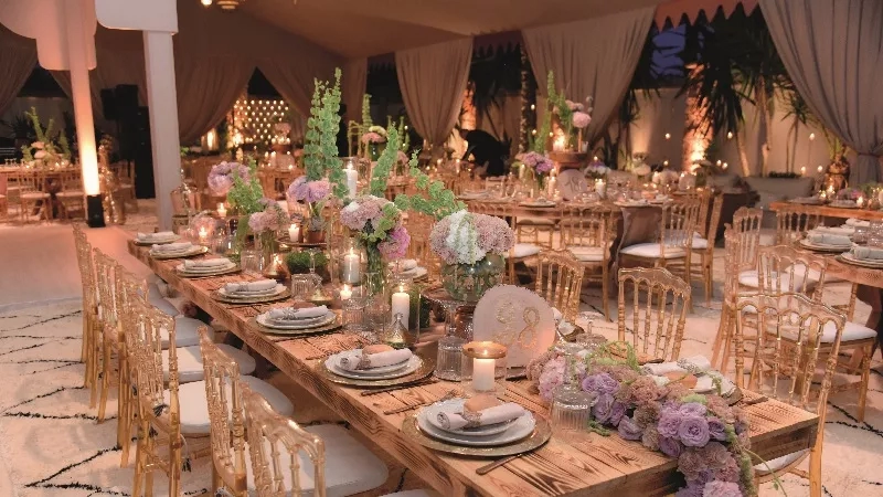 A large wooden table is set up for a banquet with candles, flowers, and plates on it.