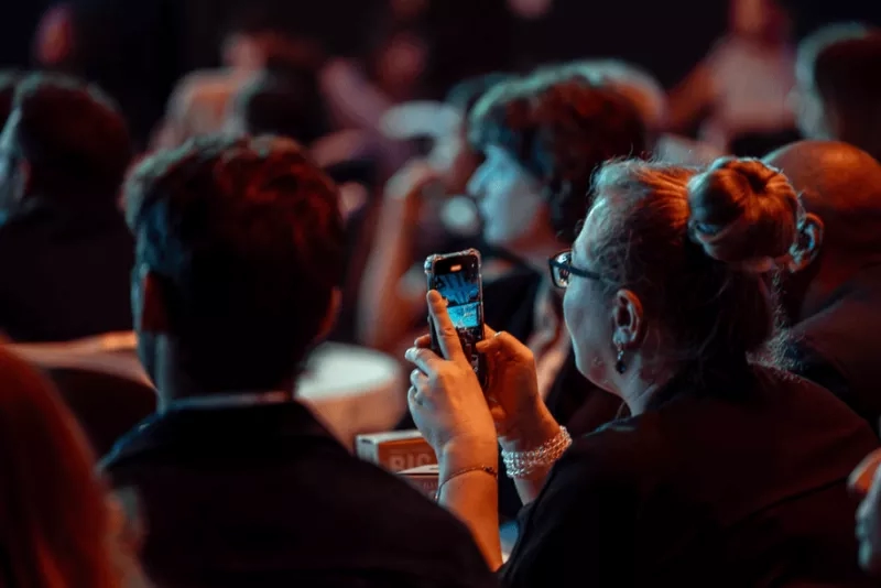Woman taking a photo of the audience with her phone at an event.