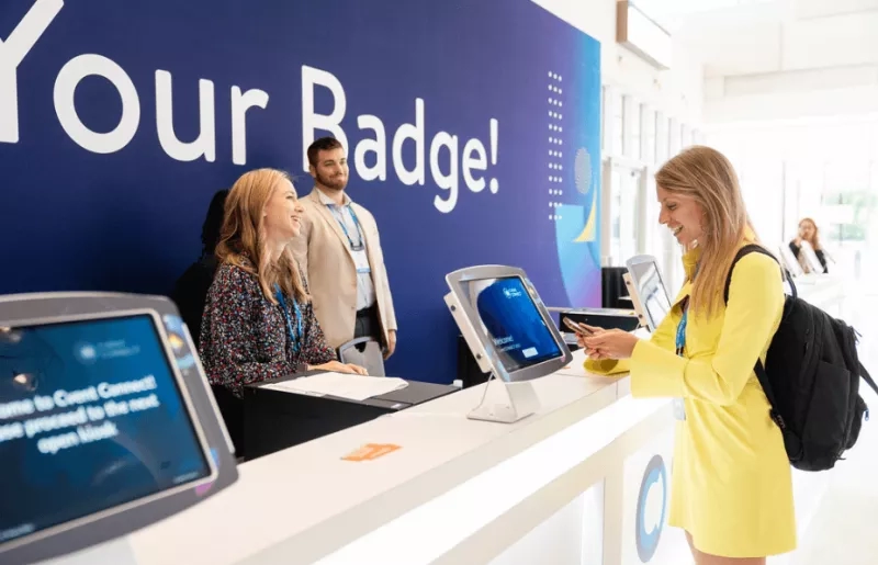 A woman scans her badge at an event check-in counter with a blue wall in the background.