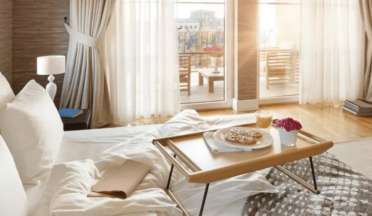 A hotel room with a tray of food and a view of the balcony through glass doors.