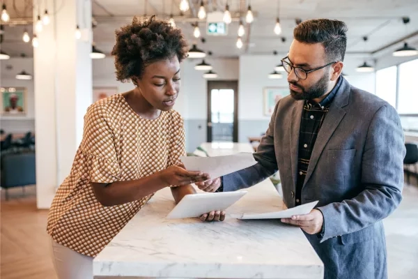 Businessman and woman reading papers on countertop in an office with warm lighting and modern architecture.