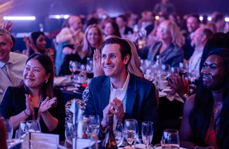 People are clapping at a meeting with bottles and glasses on the table in front of them.