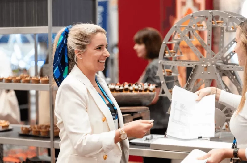 A woman is talking to another woman while giving her a paper.