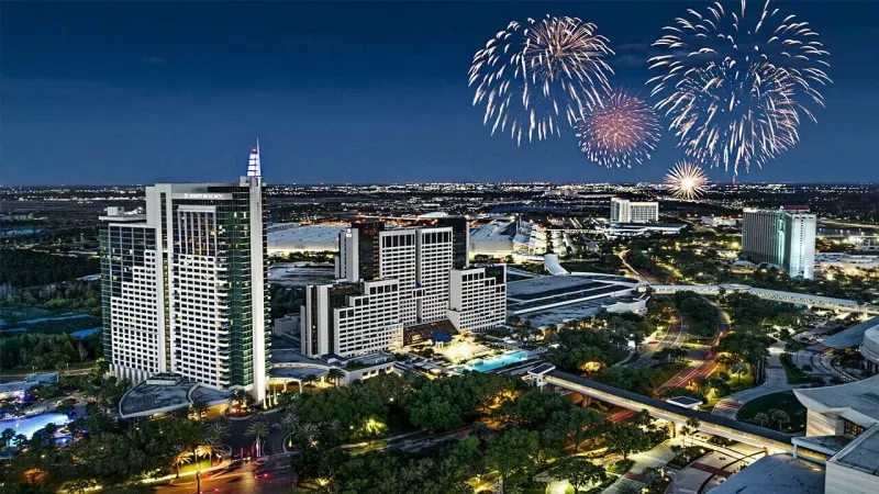 An aerial view of the city at night with fireworks, buildings, trees, and a swimming pool.