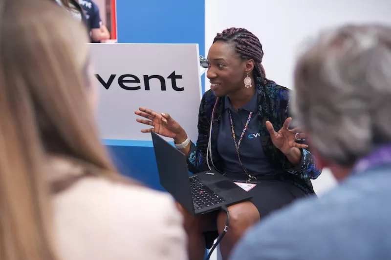 A lady is speaking to a group of people at the CVI event while holding a laptop.