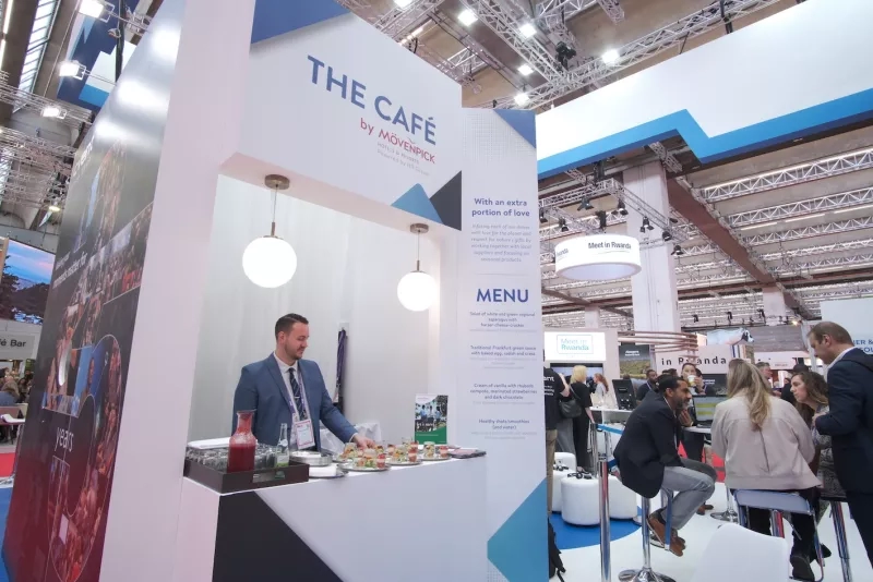 Man at a booth with a sign saying "The Cafe by Movenpick" at an event.
