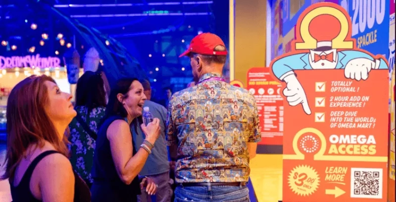 Three people are standing near the Omega Mart sign with a QR code at a gaming arcade.