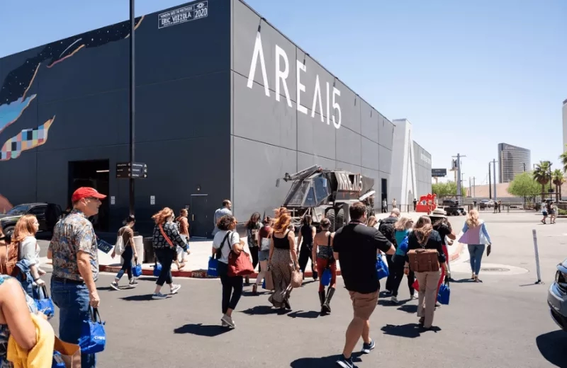 A crowd of people walking towards the Area15 building with a large mural on the wall.