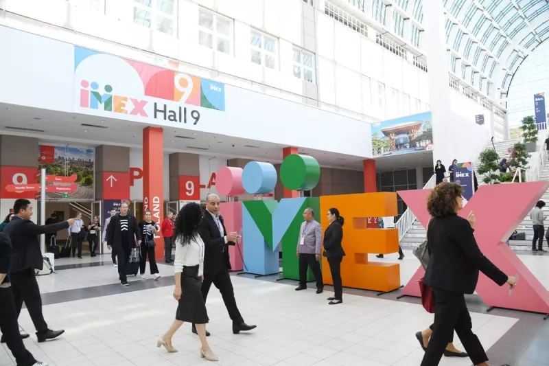 Group of people walking at IMEX Hall 9, with colorful letters and a sign for the event.
