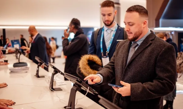 Two men at an airport looking at a tablet with a third man in the background.