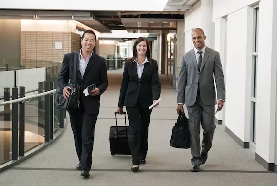 Three business travelers with their luggage walk down a hallway in the airport.