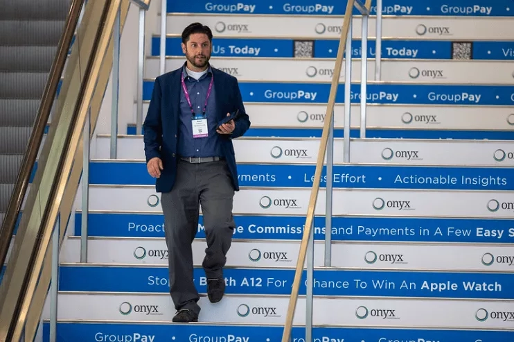 A man with an ID badge is walking up a flight of stairs with advertisements on each step.