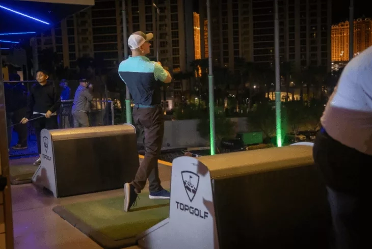 Topgolf Las Vegas, a man is swinging a golf club with other people and buildings around.