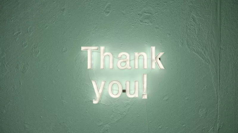 Thank you sign is illuminated in white font on the green textured wall of the hotel.