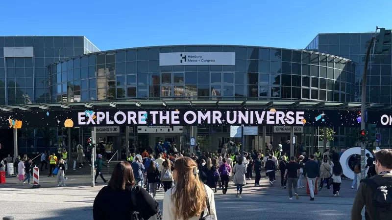 People entering the OMR Festival in a large glass building with the text "Explore the OMR Universe."