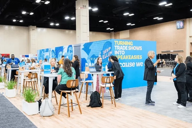 People conversing at the TS ROI event, with a blue wall in the background that says "Turning Trade Shows Into Speakeasies."