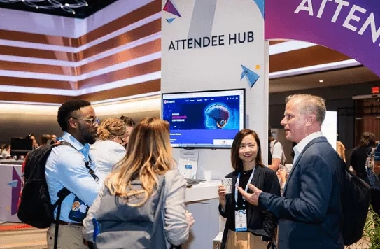 People at a trade show with a sign behind them reading "Attendee Hub" in purple and white.