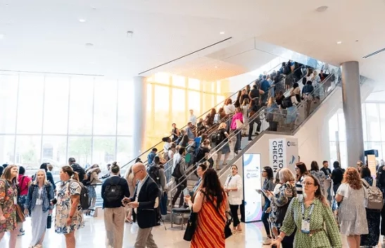 Several people are standing on the floor and stairs in an event hall with glass walls and doors.