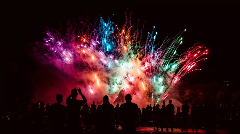 A crowd of people is watching the fireworks display at night, with a colorful display of fireworks.