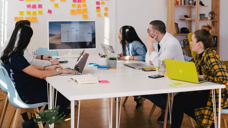 Team of four working at a desk with laptops and a monitor at a briefing.