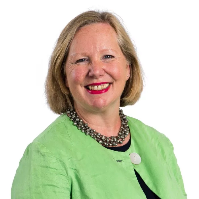 Jacky Griffiths, a woman with blonde hair wearing a green blazer and pearl necklace, smiling at the camera.