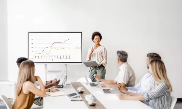 A group of people are sitting in front of a woman giving a presentation.