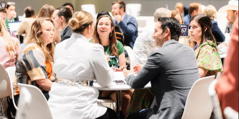 A group of people at a meeting, some wearing name tags, having a discussion at tables.