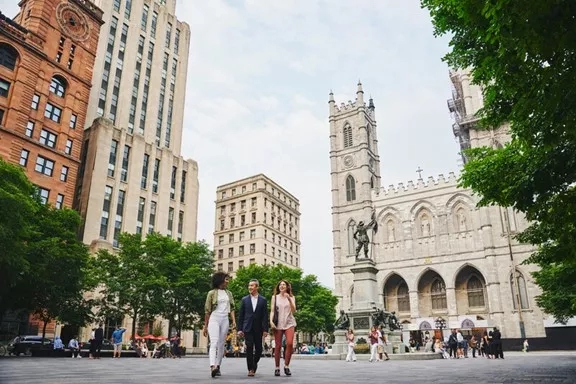 A group of people walking past Montreal cathedral in downtown Montreal with trees and large buildings around.