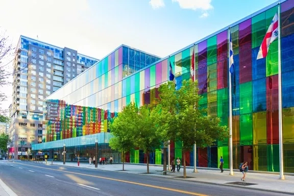 The exterior of the Place des Arts building with vibrant windows and flags on a sunny day.