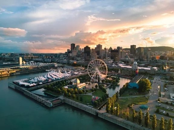 Aerial view of Montreal city with Ferris wheel, water body, and buildings during a cloudy sunset.