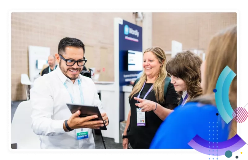 Three people at a trade show with one man holding a tablet and talking to two women.