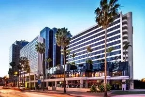 Hotel exterior shot at dusk with palm trees and a street in front of the building.