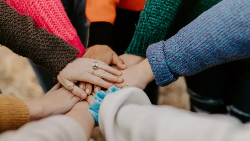 Several people are holding hands in a circle in the outdoors in a park.