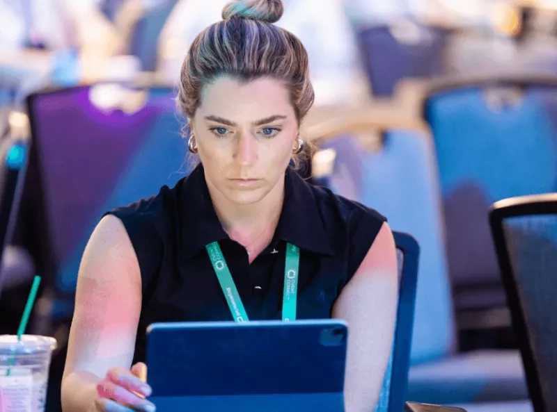 A woman in black shirt is sitting on chair in front of laptop with many chairs in background.