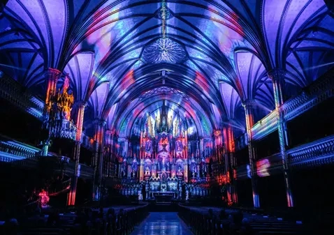 The interior of the Notre-Dame Basilica with vibrant lights and an audience sitting in the pews.